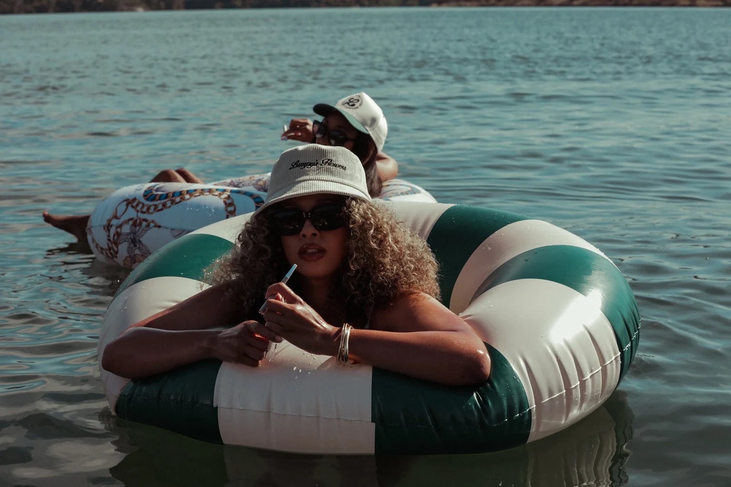 Two friends on striped pool floats wearing Lumpy's corduroy hats on a lake